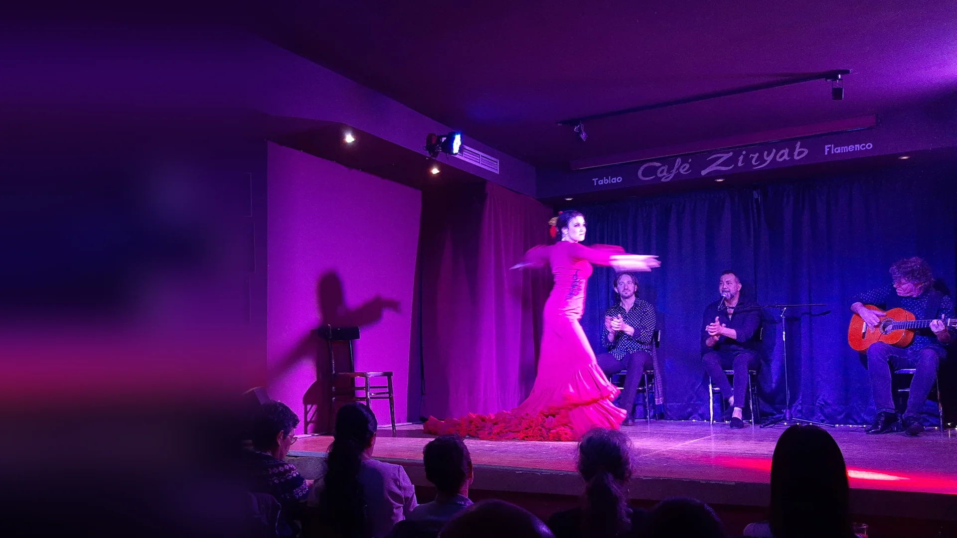 En danser i fuchsiafarvet kjole midt i en drejning på den lille scene på Café Ziryab i Madrid, med to siddende kunstnere, der klapper, og en guitarist til højre